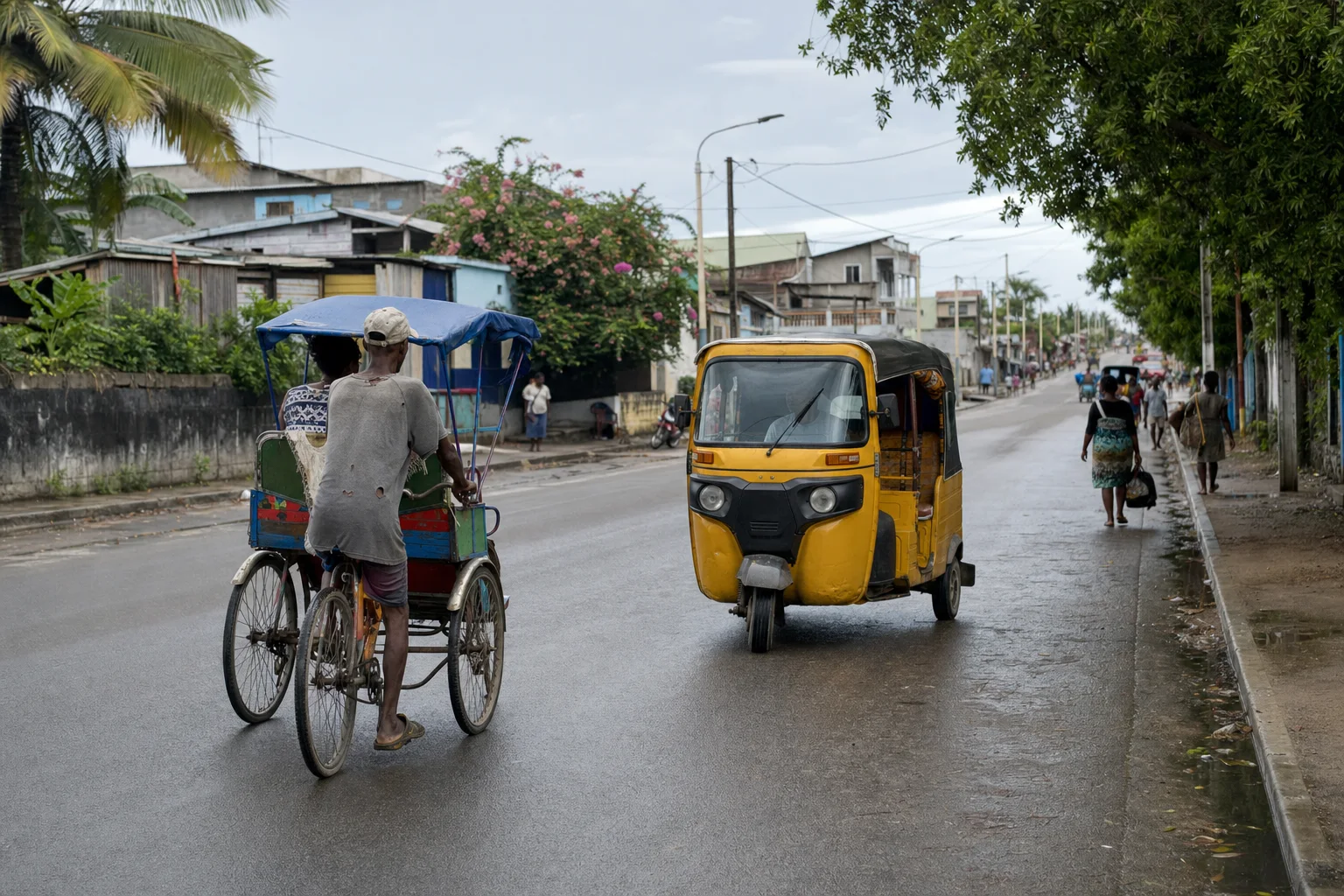 Pousse-pousse à pédales et tricycle motorisé dans une rue de Toamasina après la pluie